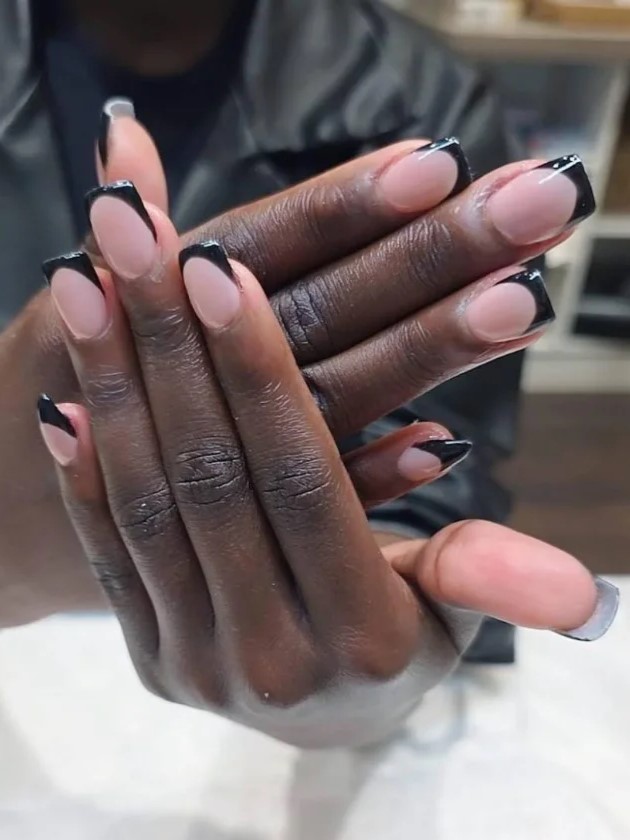 Frau im Nagelstudio zeigt ihre nude BIAB-Maniküre mit schwarzen Verlängerungen in die Kamera