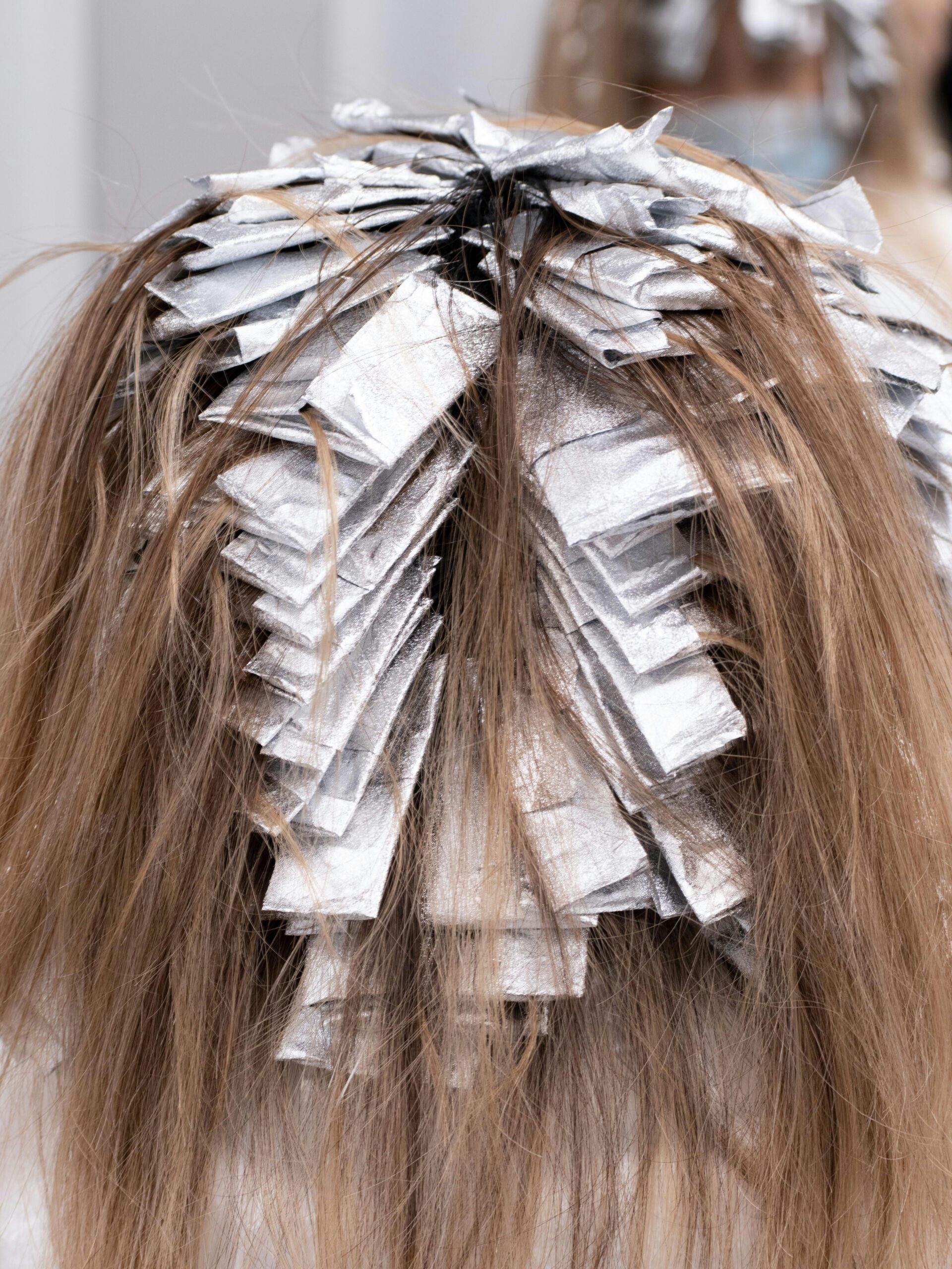 Hinterkopf einer Kundin mit Folien im Haar während einer Teilcoloration beim Friseur