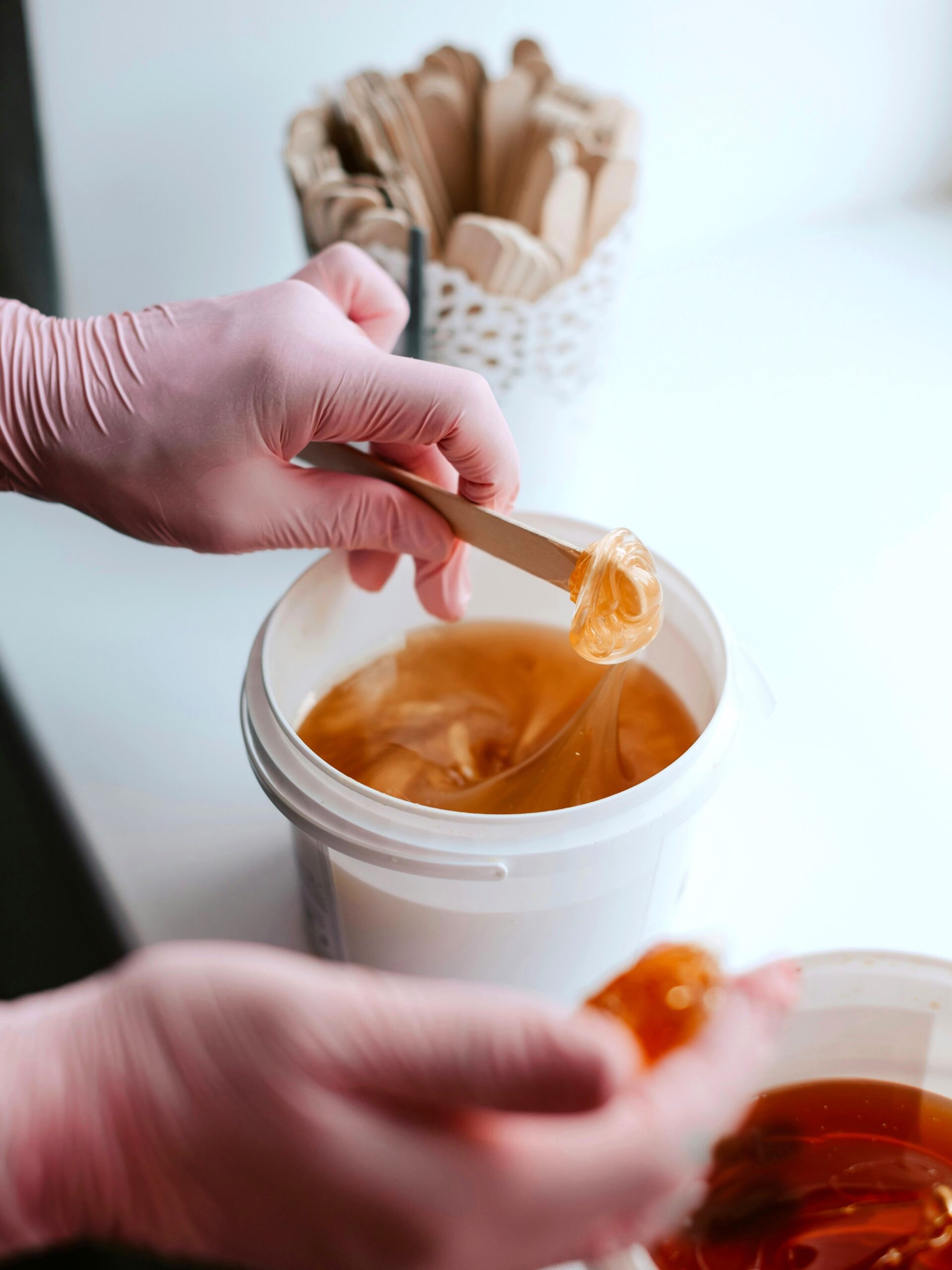 Nahaufnahme von zwei Töpfchen Zuckerpaste, während eine Kosmetikerin mit einem Spatel Wachs entnimmt