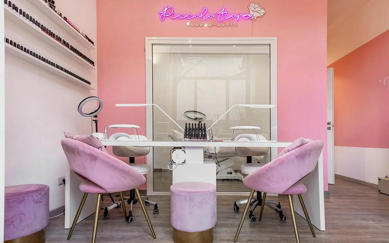 Eine lebhafte Maniküre-Station mit knallpinken Wänden und einem pinkfarbenen Neonschild. Fliederfarbene Samtstühle mit goldenen Beinen stehen an einem minimalistischen weißen Tisch mit professionellen LED-Nagellampen.