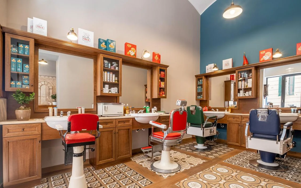 Ein hochwertiger, traditioneller Barbershop mit edler Holzvertäfelung, gemusterten Vintage-Bodenfliesen und professionellen Barbierstühlen in Rot, Grün und Marineblau. Traditionelle Pflegeprodukte stehen auf den Regaleinheiten.