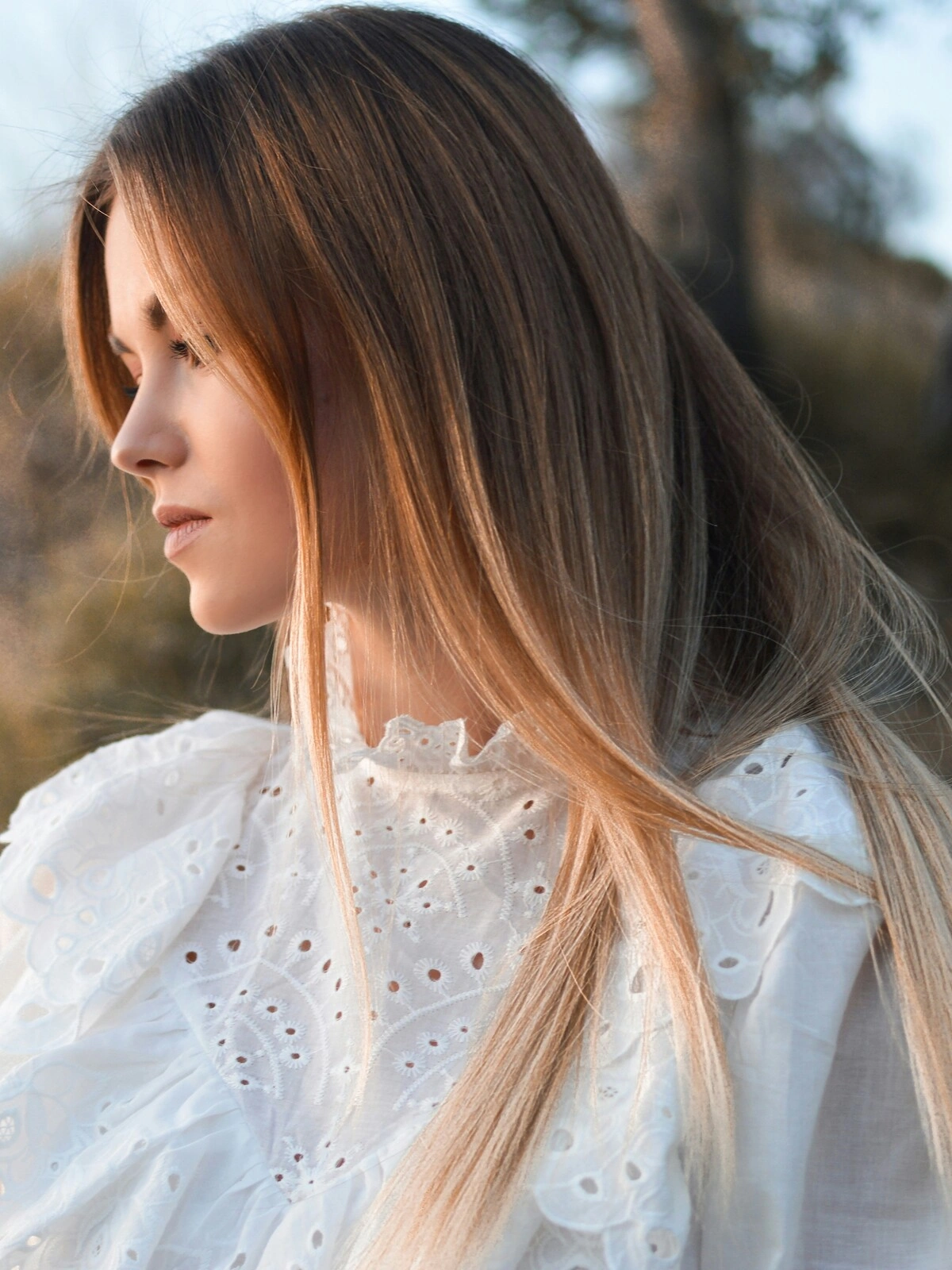 Seitenansicht einer Frau im Freien in natürlicher Umgebung mit glatter Balayage, bei der brünettes Haar in blonde Nuancen übergeht