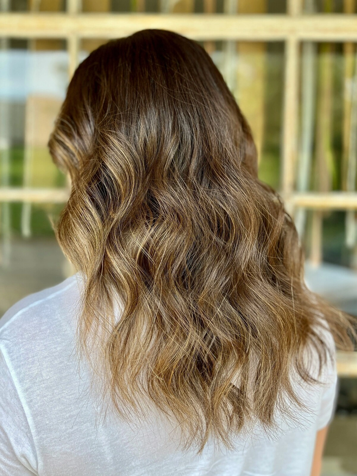 Rückansicht des Kopfes einer Frau mit welliger Balayage, bei der dunkles Haar in warme Töne übergeht
