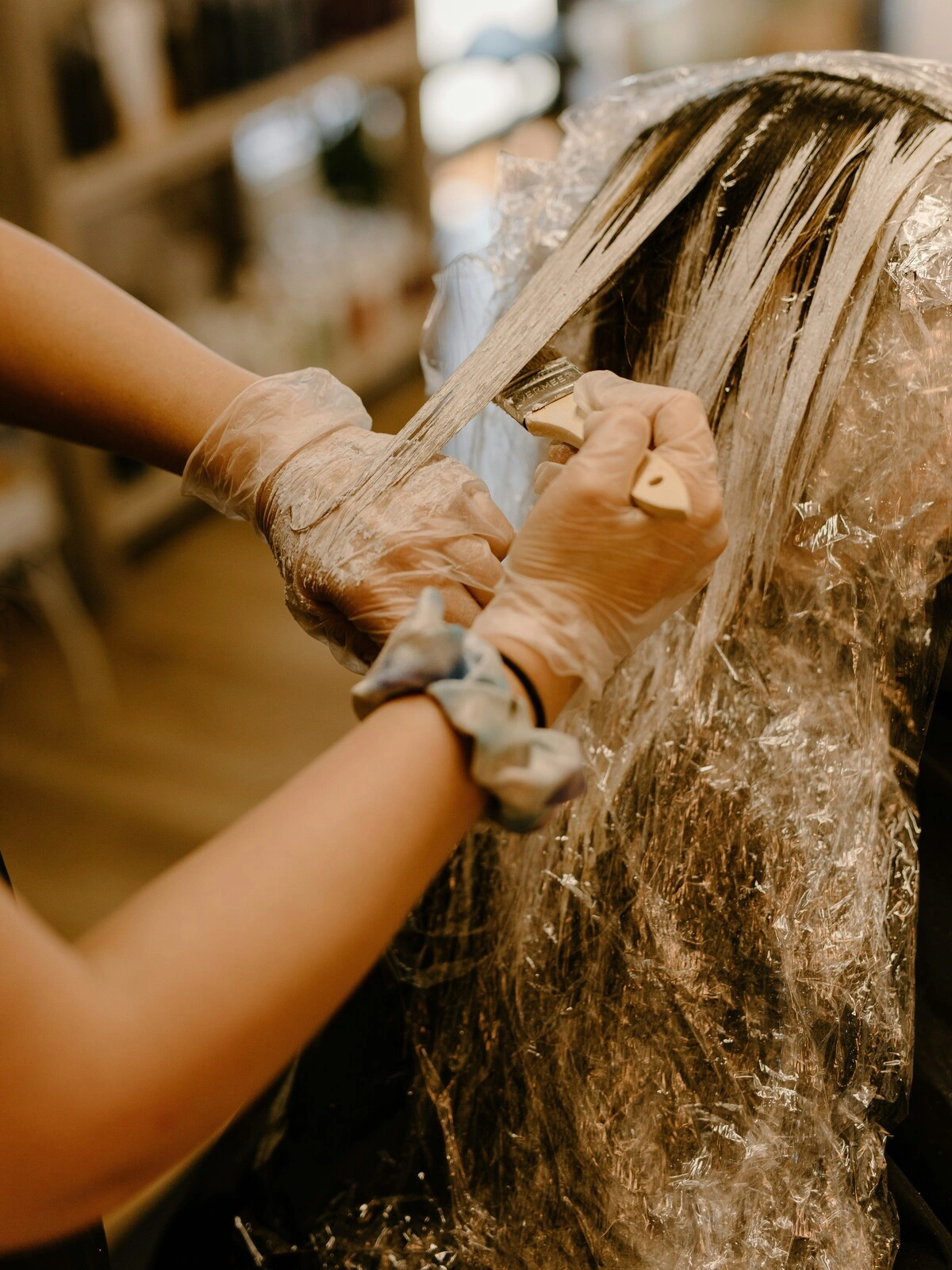 Eine Coloristin mit Handschuhen trägt mit einem Pinsel Farbe ins Haar einer Kundin auf, als Teil einer Balayage-Behandlung