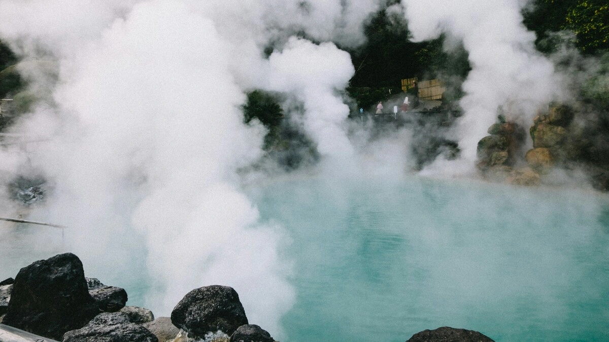 Weite Ansicht heißer Quellen in Japan, mit Dampfschwaden, die von einem von Felsen und Grün umgebenen Becken aufsteigen