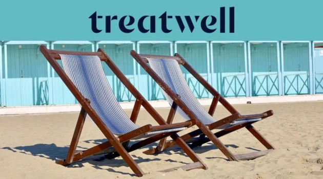 Zwei gestreifte Holzliegestühle im Sand vor pastellblauen Strandkabinen an der Küste der Versilia