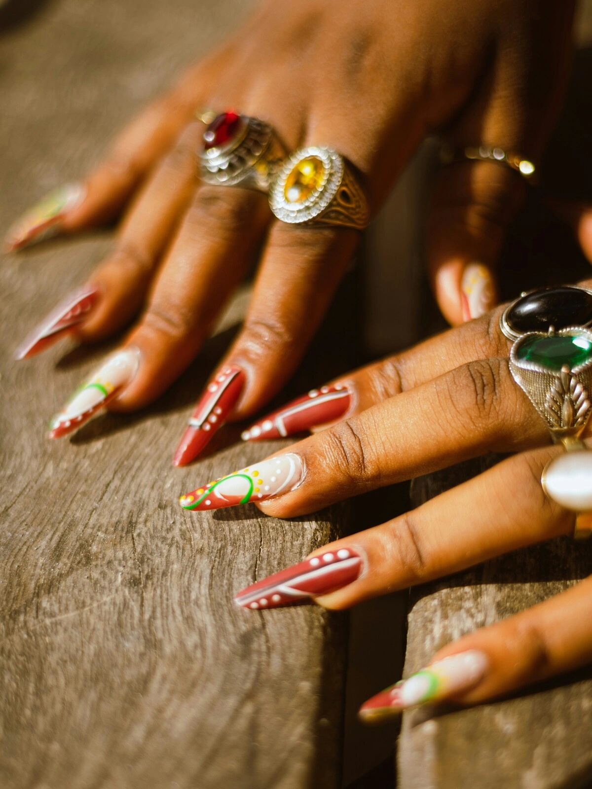 Nahaufnahme der Hände einer Frau mit Acrylnägeln in Stiletto-Form in Rot und Weiß, verziert mit grünen und gelben Punkten und Schwüngen