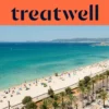 Luftaufnahme der Playa de Palma auf Mallorca, mit einem langen, geschwungenen Streifen goldenen Sandes, Reihen von Sonnenschirmen, ruhigem türkisfarbenem Wasser und einer palmengesäumten Promenade entlang der Stadt, mit Hügeln in der Ferne unter klarem blauem Himmel.