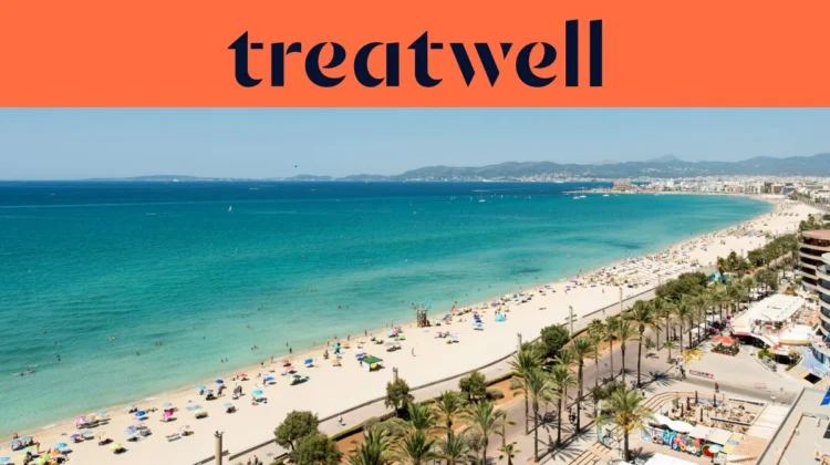 Luftaufnahme der Playa de Palma auf Mallorca, mit einem langen, geschwungenen Streifen goldenen Sandes, Reihen von Sonnenschirmen, ruhigem türkisfarbenem Wasser und einer palmengesäumten Promenade entlang der Stadt, mit Hügeln in der Ferne unter klarem blauem Himmel.