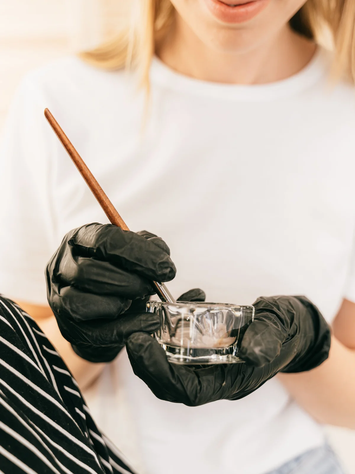 Nahaufnahme einer Kosmetikerin, die ein kleines Glasschälchen und einen feinen Pinsel hält und im Salon Augenbrauenfarbe anmischt