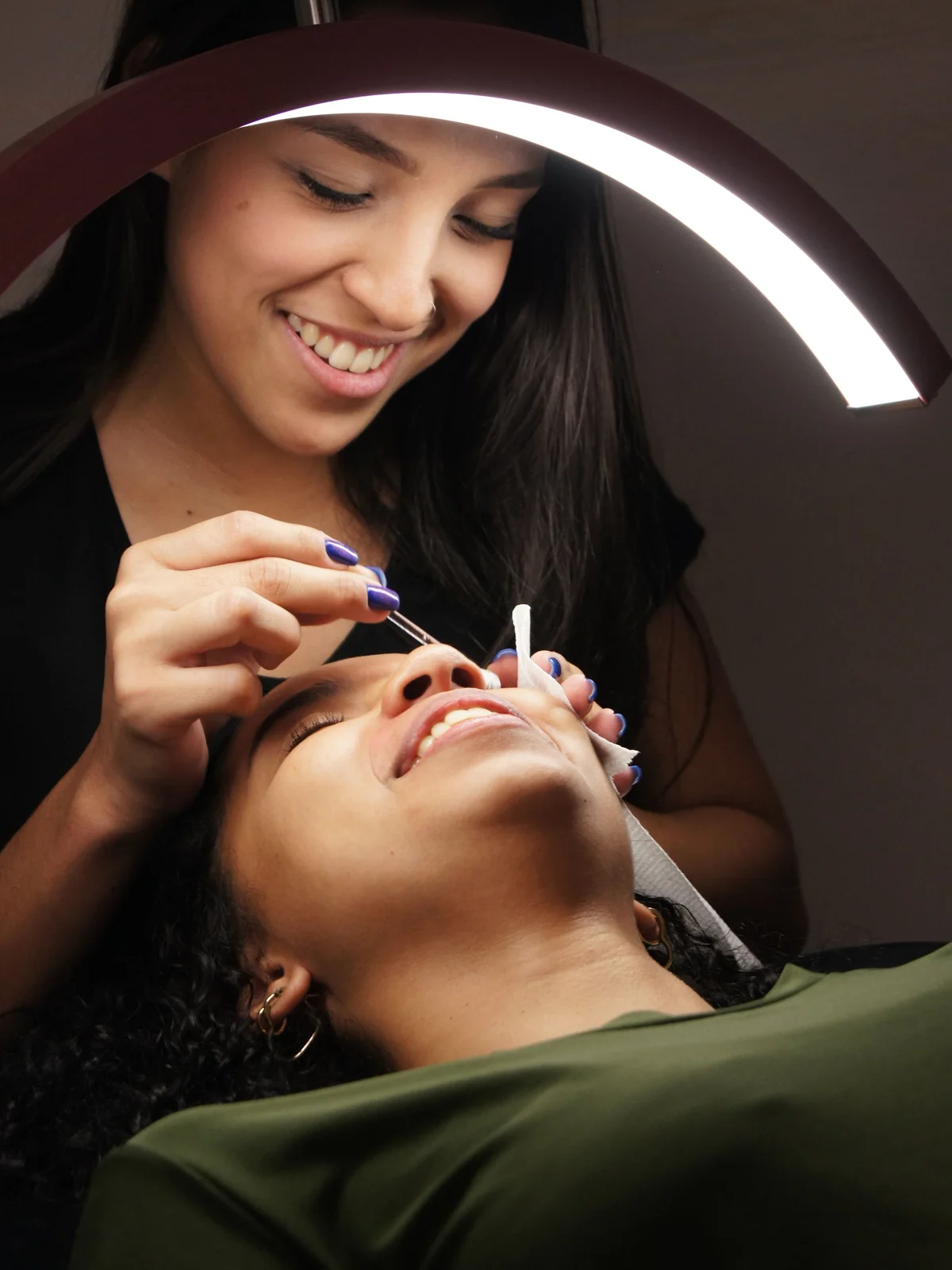 Nahaufnahme einer Kosmetikerin, die einer entspannt auf der Behandlungsliege liegenden Kundin im Salon die Augenbrauenfarbe aufträgt