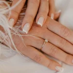 Klassische weiße French-Tip-Maniküre auf naturbelassenen, eckig gefeilten Nägeln auf weißem Stoff