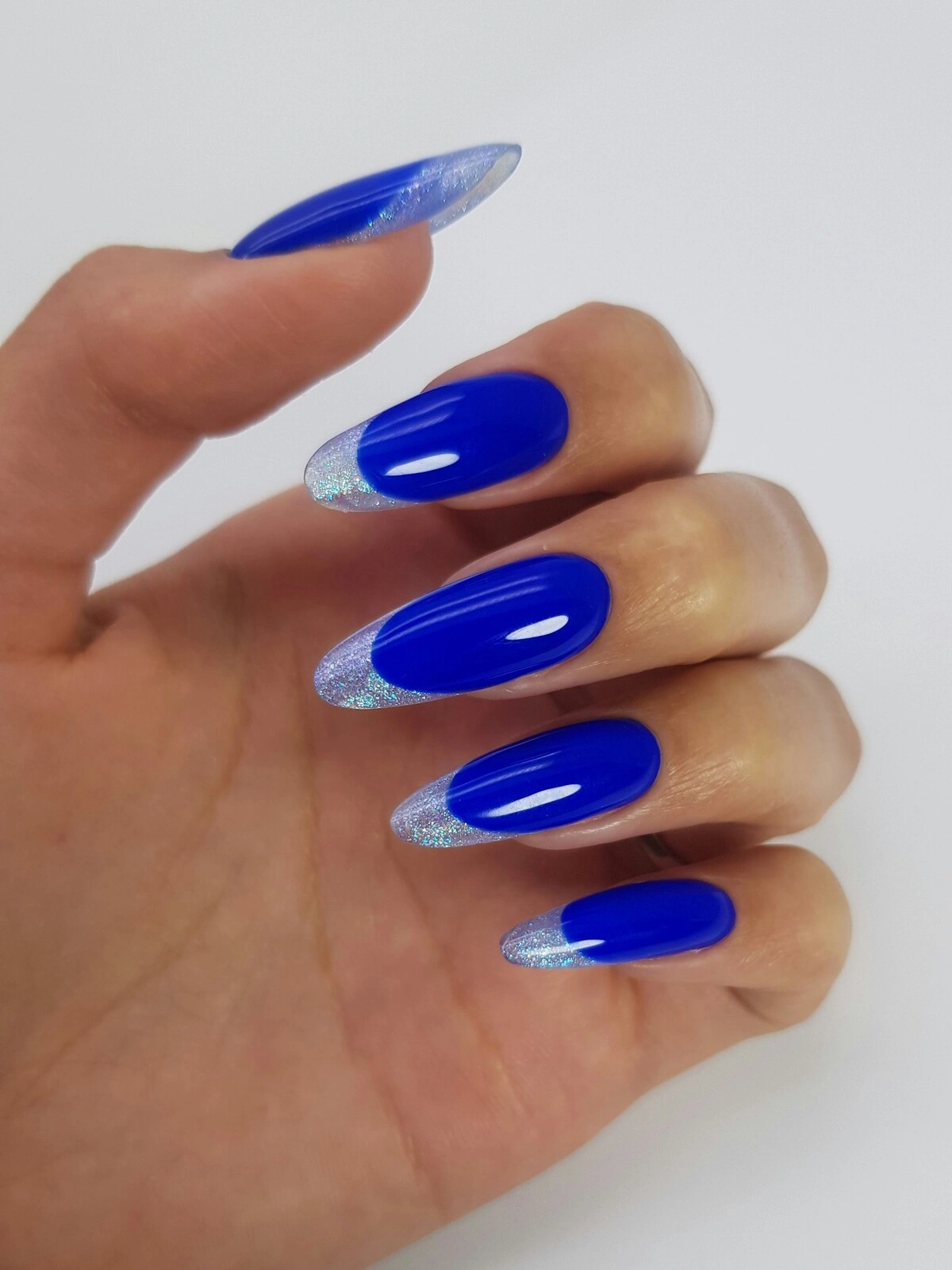 Die Hand einer Frau mit einer auffälligen French-Tips-Maniküre mit knallblauer Basis und silbernen Metallic-Spitzen auf langen, mandelförmigen Nägeln