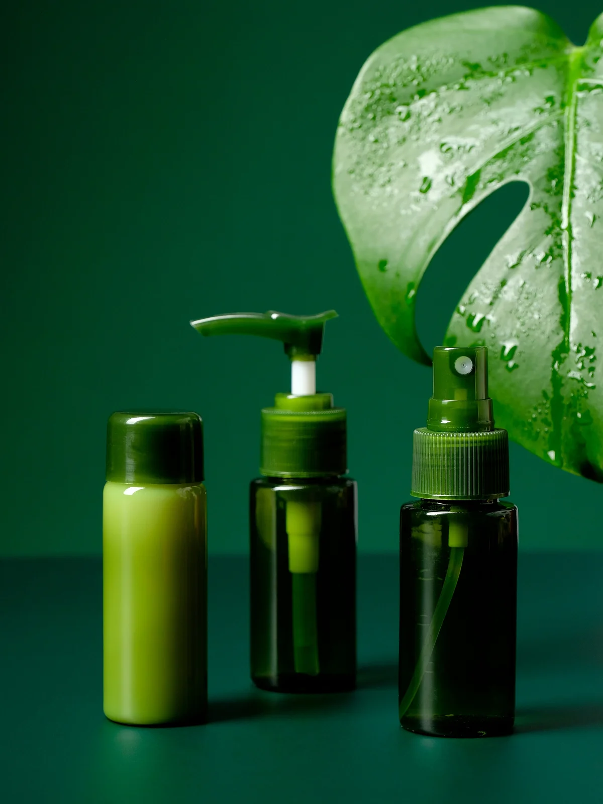 Produktaufnahme von drei beruhigenden Gels und Cremes in grünen Flaschen mit einem großen tropischen grünen Blatt im Hintergrund