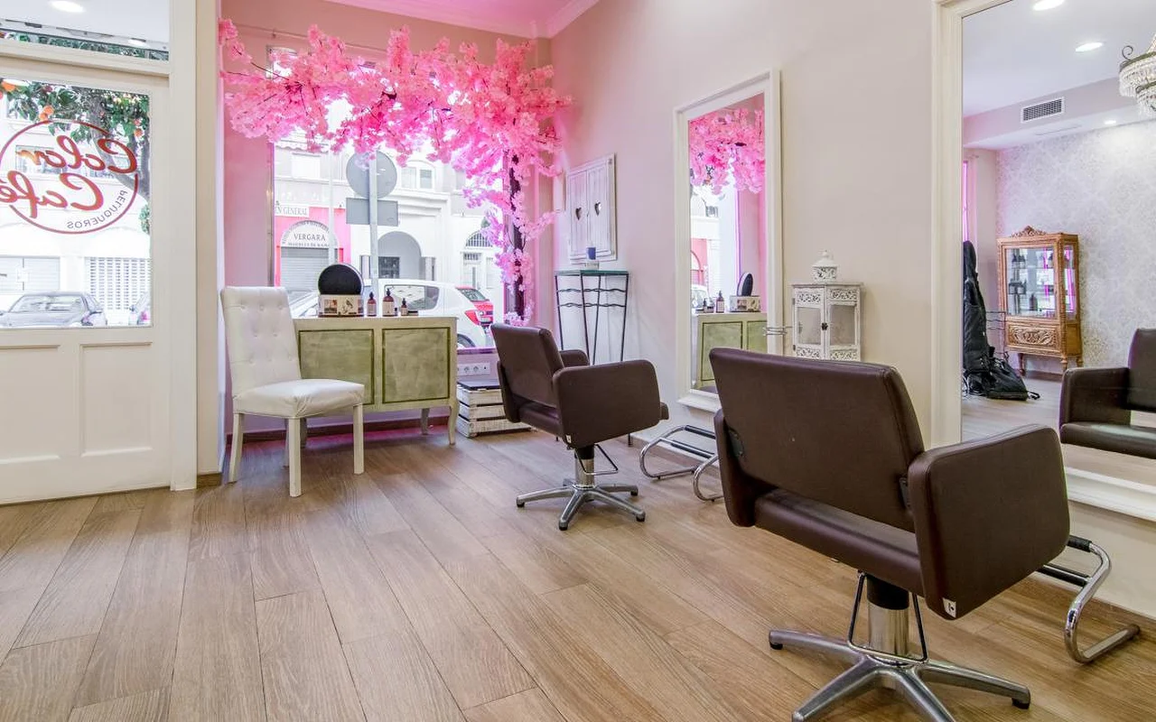 Das Innere von Color Café Peluqueros in Torremolinos, ein Friseursalon mit rosa Wänden, braunen Styling-Stühlen, großen Spiegeln und einer rosa Kirschblüten-Deko im Schaufenster.