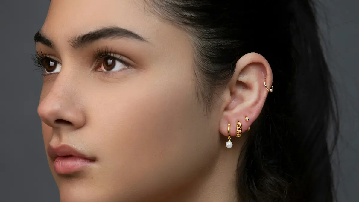 Studioaufnahme einer Frau mit einem Curated Ear aus mehreren Ohrläppchen-Piercings und einem Helix-Ring