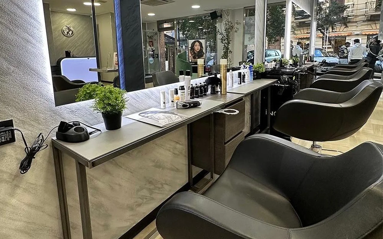Der Styling-Bereich von Equipe Beauty, mit einer Reihe schwarzer Stühle entlang einer Theke in Marmoroptik, einem großen hinterleuchteten Spiegel, Styling-Produkten und einer Topfpflanze auf der Theke, und raumhohen Fenstern zur Straße.