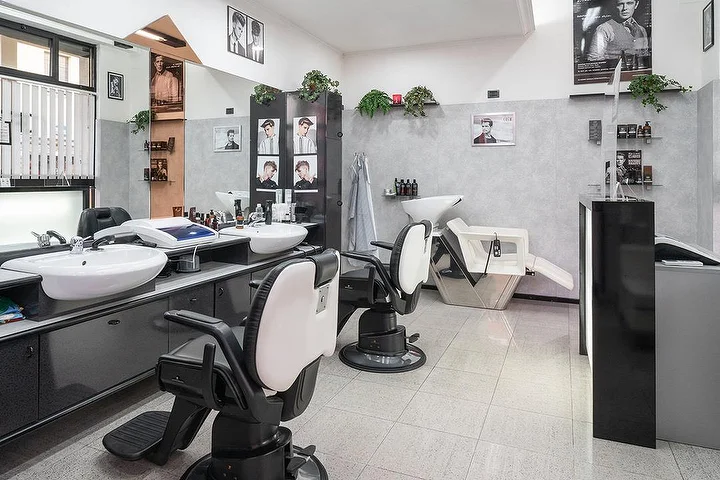 Vintage-Barber-Stühle und Waschplätze bei Fabio Desole Acconciature Maschili in Sassari mit gerahmten Porträts an den Wänden.