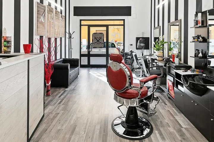 Roter Vintage-Barber-Stuhl im Hair 99 in Alghero mit den markanten schwarz-weiß gestreiften Wänden.