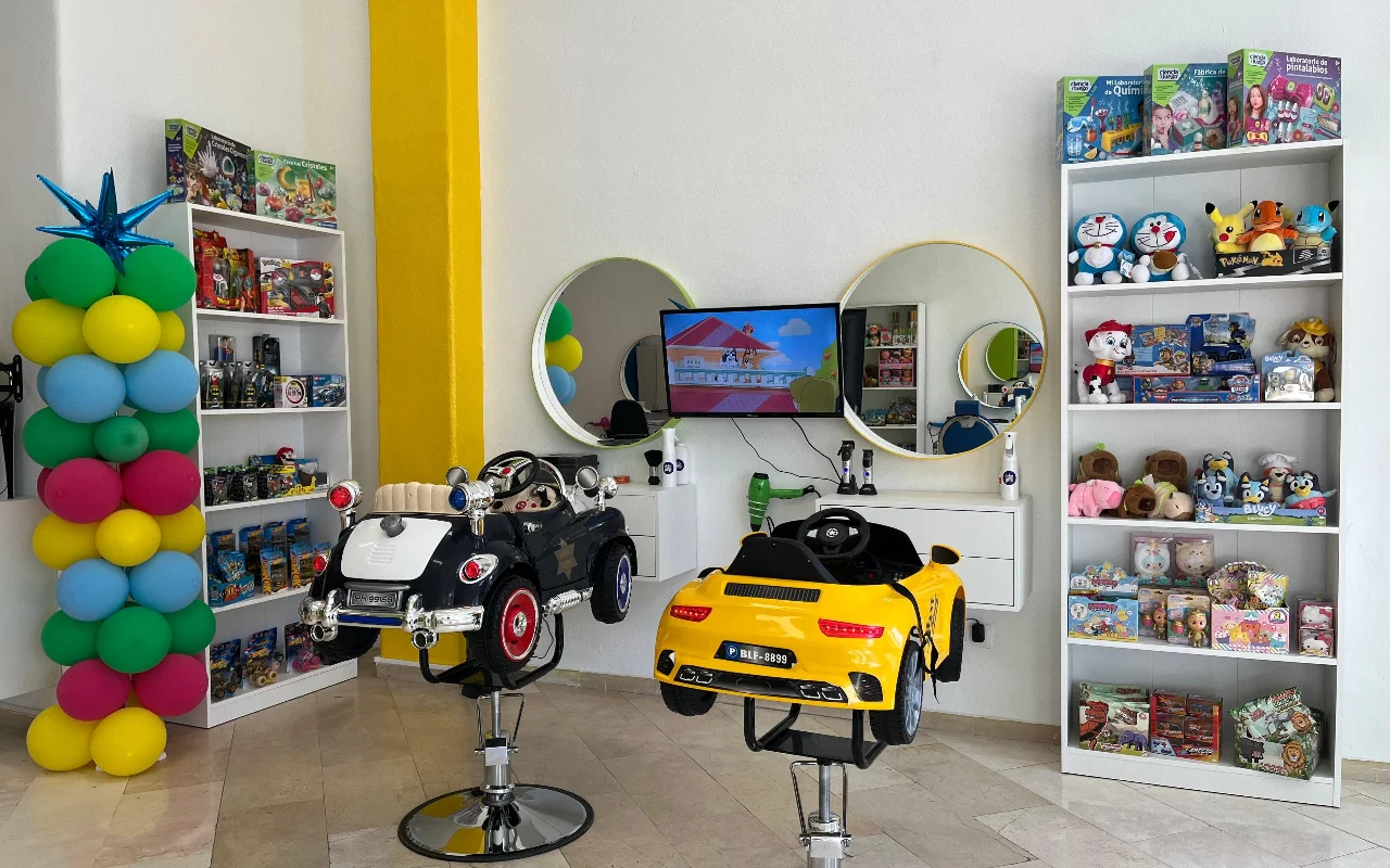 Der Kinderbereich von Peluplay in Benalmádena, wo die Styling-Stühle wie Spielzeugautos geformt sind, mit Regalen voller Zeichentrickfiguren, runden Spiegeln und einer Ballonsäule.