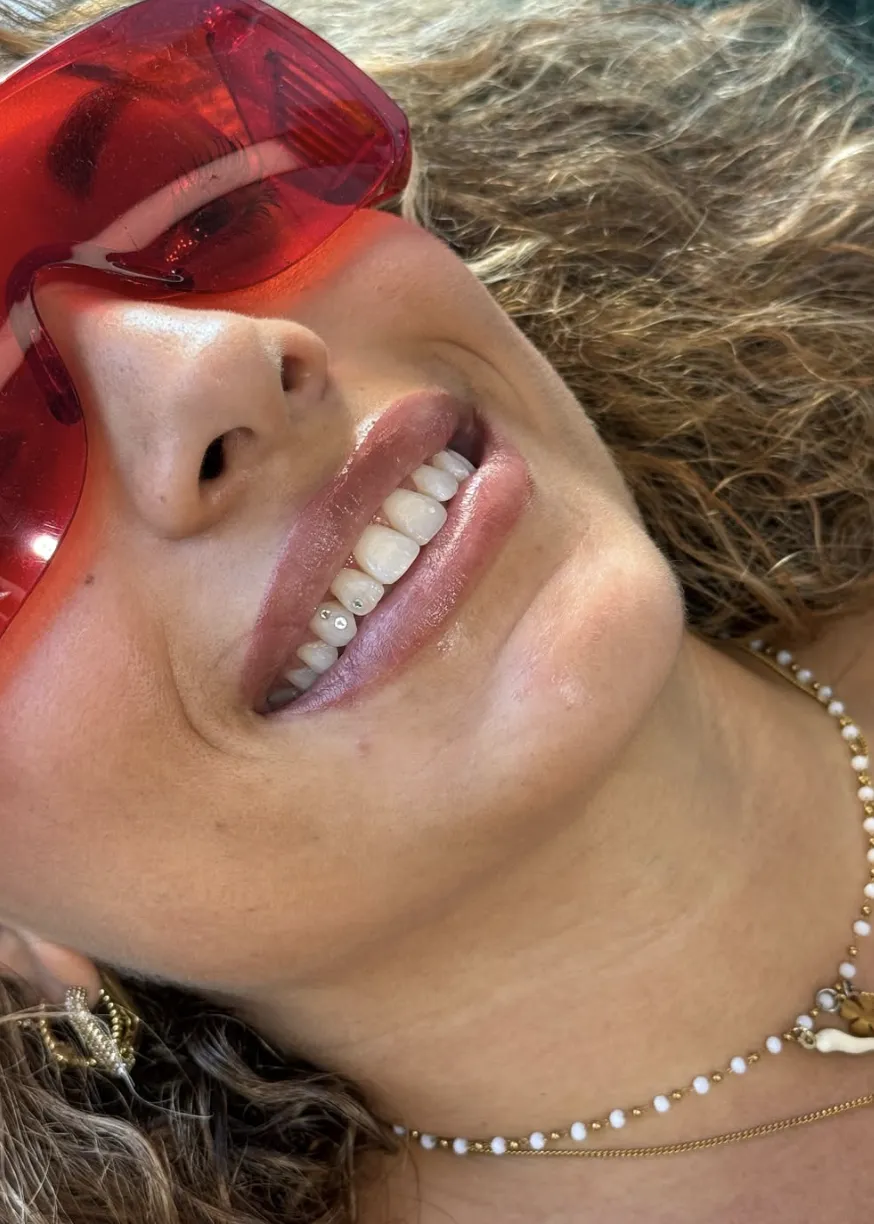 Nahaufnahme eines Lächelns mit zwei kleinen Kristall-Tooth-Gems auf den unteren Zähnen, sommerliches Porträt