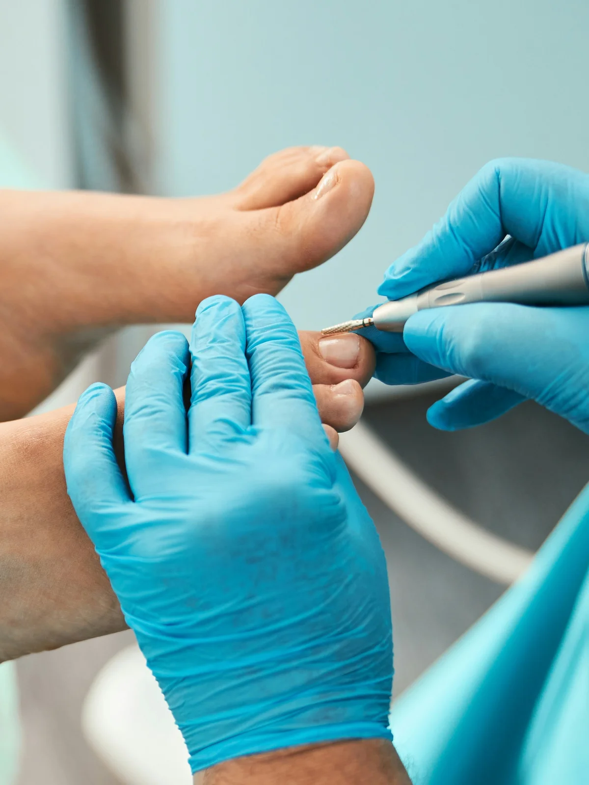 Nahaufnahme einer Fachkraft mit Handschuh, die mit einem kleinen Werkzeug die Nagelhaut an den Zehen einer Kundin zurückarbeitet