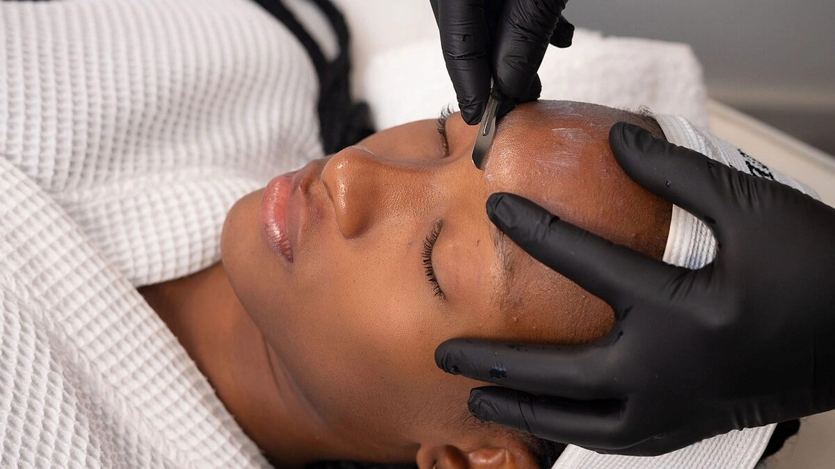 Nahaufnahme einer Kosmetikerin, die bei einer Kundin im Salon ein Dermaplaning durchführt
