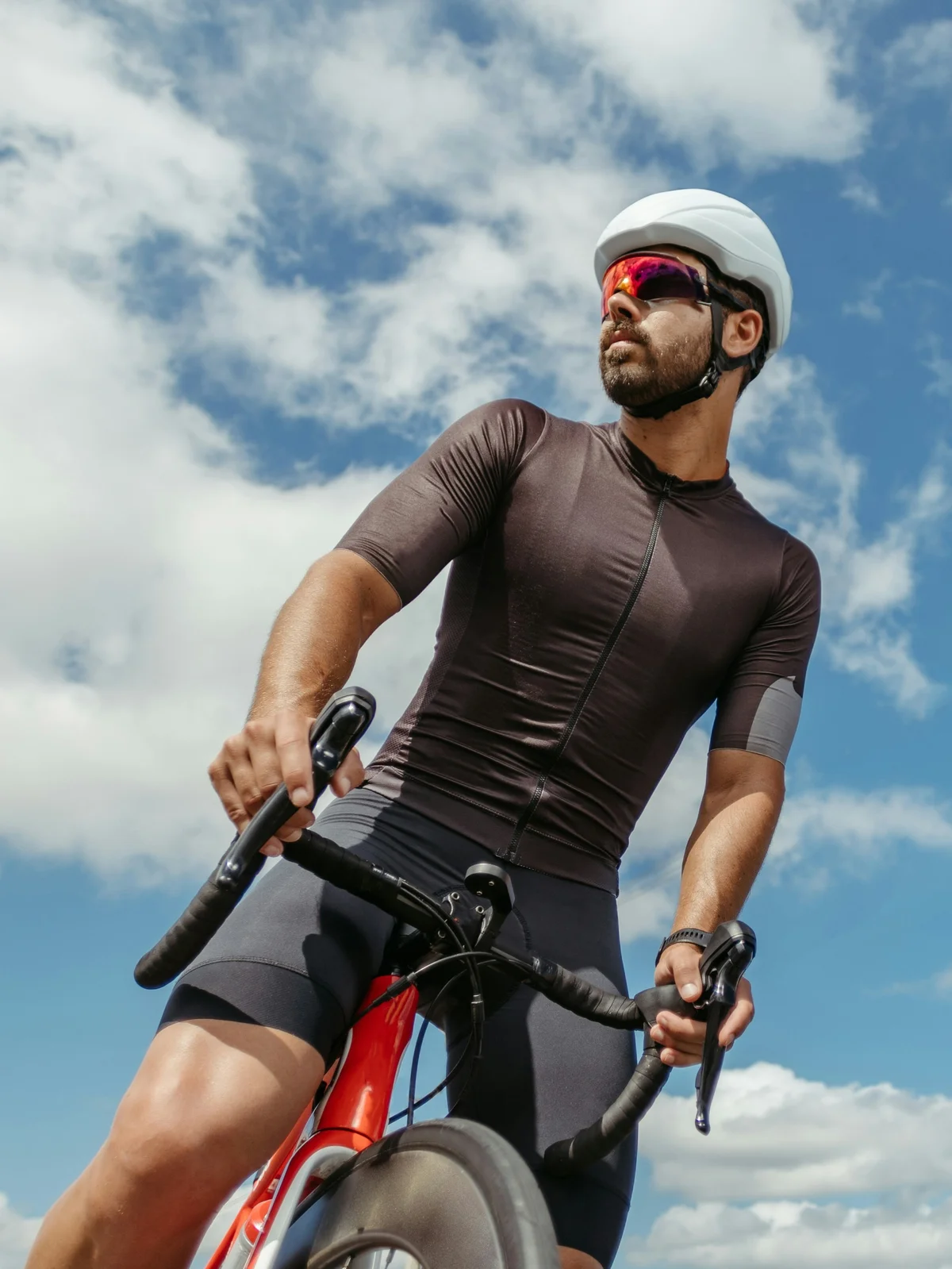 Aus der Froschperspektive: Ein Rennradfahrer sitzt auf seinem Rad und blickt sich unter einem blauen Himmel mit Wolken um