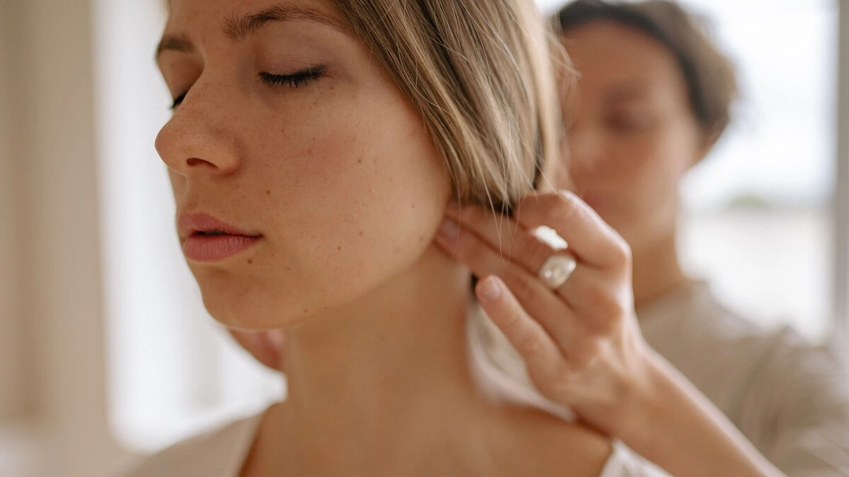 Nahaufnahme einer Frau mit geschlossenen Augen, während eine Fachkraft bei einer indischen Kopfmassage mit den Händen Druck auf ihren Hinterkopf ausübt